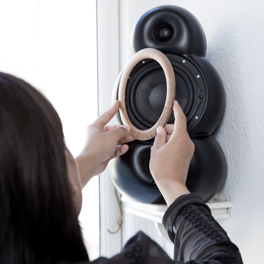 A person is attaching a wooden decoration ring with magnets to a black Scandyna MNP MK4 loudspeaker.